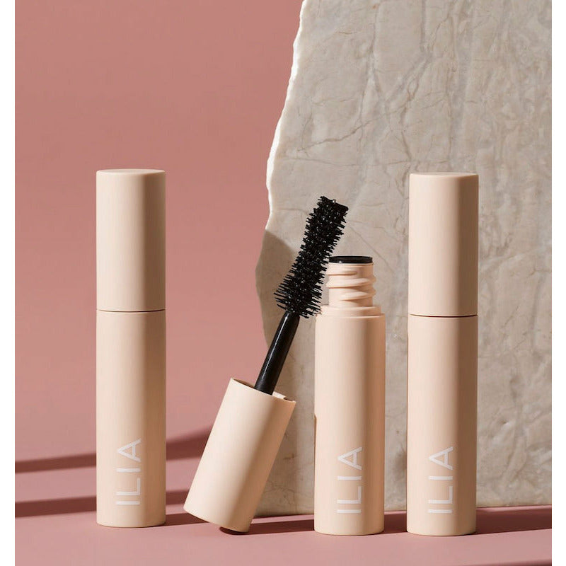 Makeup mascara products from ilia brand displayed against a marble and pink background.