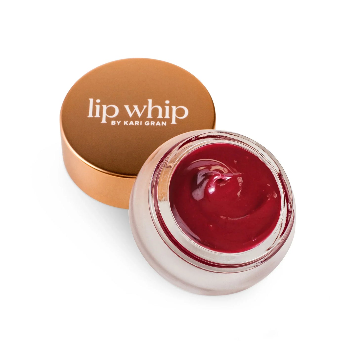 A jar of red-tinted lip whip next to its bronze-colored lid.